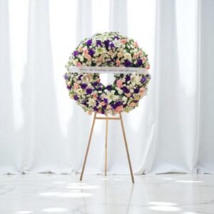 Corona fúnebre con flores lisianthus rosa y morado sobre caballete de madera, ideal para expresar condolencias con elegancia y ternura.