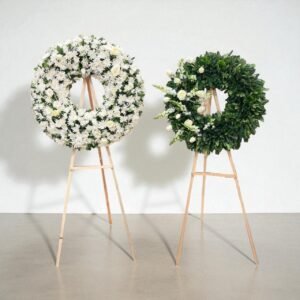 Paquete de dos coronas fúnebres con flores blancas y follaje verde sobre caballetes de madera.