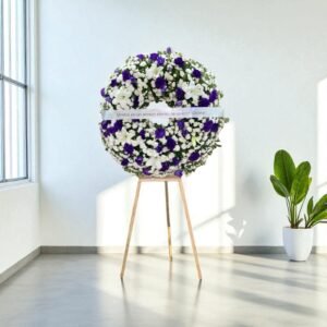 Corona fúnebre con flores moradas y blancas sobre caballete de madera, ideal para expresar condolencias con elegancia.