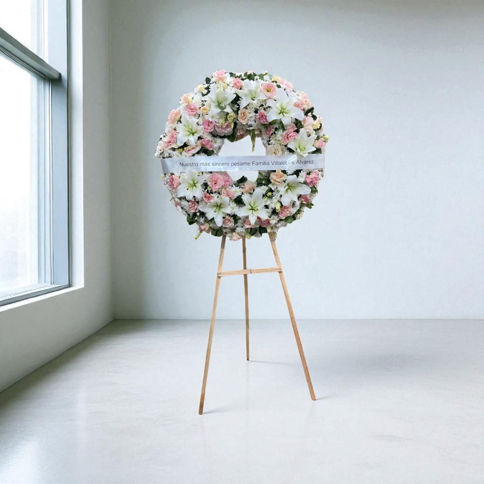 Corona fúnebre con flores blancas y rosas sobre caballete de madera, ideal para expresar condolencias con elegancia.