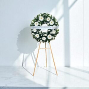 Corona fúnebre chica con flores blancas sobre caballete de madera, ideal para expresar condolencias con sencillez.